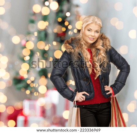 happiness, winter holidays and people concept - smiling young woman in winter clothes with shopping bags over christmas tree background