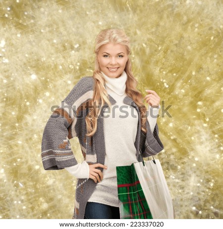 happiness, winter holidays, christmas and people concept - smiling young woman in winter clothes with shopping bags over yellow lights background