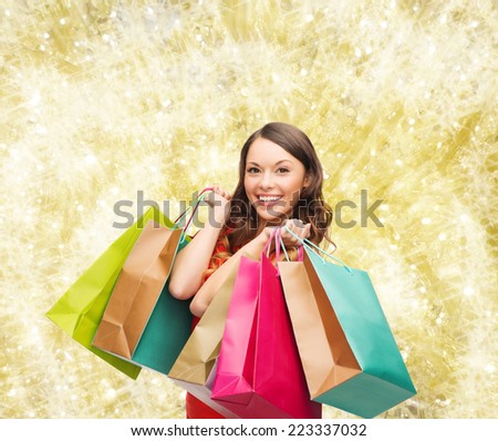 sale, gifts, christmas, holidays and people concept - smiling woman with colorful shopping bags over yellow lights background