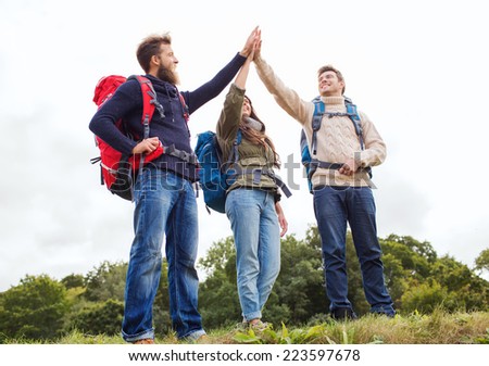 travel, tourism, hike, gesture and people concept - group of smiling friends with backpacks making high five outdoors
