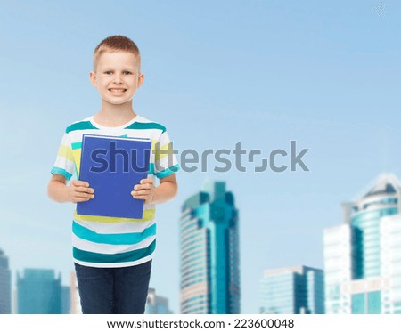 education, childhood and school concept - smiling little student boy with blue book over city background