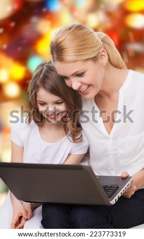 family, childhood, holidays, technology and people concept - smiling mother and little girl with laptop computer over red lights background