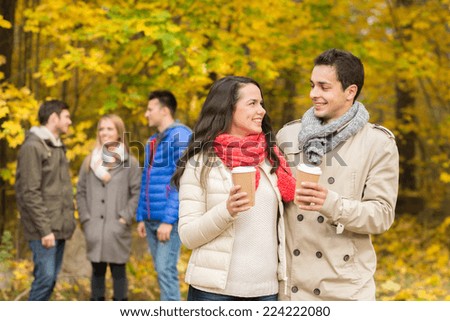 love, relationship, season, friendship and people concept - group of smiling men and women walking with paper coffee cups in autumn park