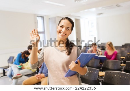 education, high school, gesture, teamwork and people concept - group of smiling students with notepads waving hand in lecture hall