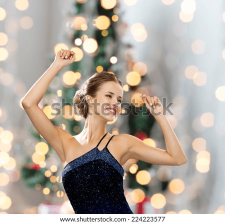people, party, holidays and glamour concept - smiling woman dancing with raised hands over christmas tree lights background
