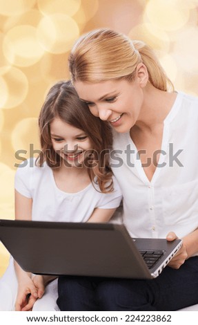 family, childhood, holidays, technology and people concept - smiling mother and little girl with laptop computer over beige lights background