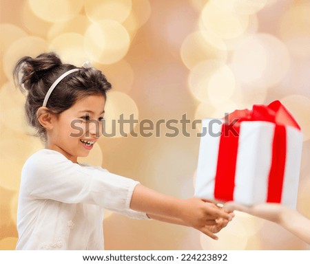 holidays, presents, christmas, childhood and people concept - smiling little girl with gift box over beige lights background