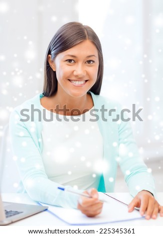 education, winter, technology and people concept - smiling young woman with laptop computer and notebook indoors