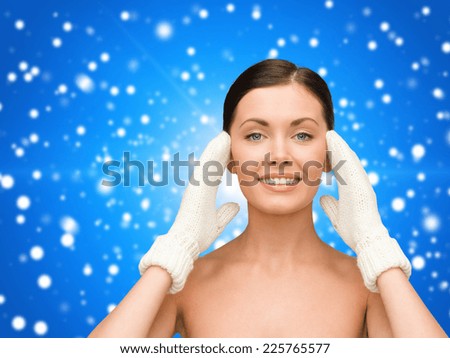 beauty, winter, people and health concept - smiling young woman in white mittens over blue snowy background