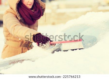 transportation, winter and vehicle concept - closeup woman cleaning snow from car back window with brush