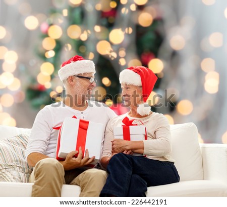family, holidays, christmas, age and people concept - happy senior couple in santa helper hats with gift boxes over tree lights background