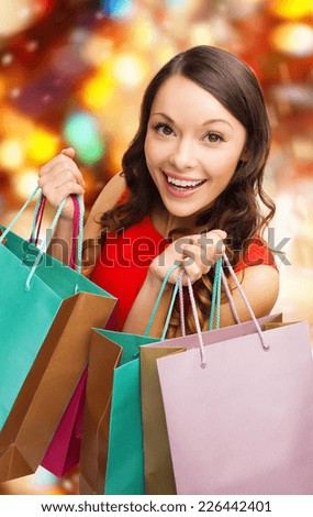 sale, gifts, christmas, holidays and people concept - smiling woman with colorful shopping bags over red lights background