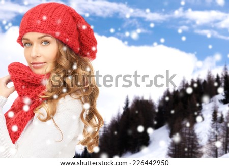 happiness, winter holidays, christmas and people concept - young woman in red hat and scarf over snowy mountains background