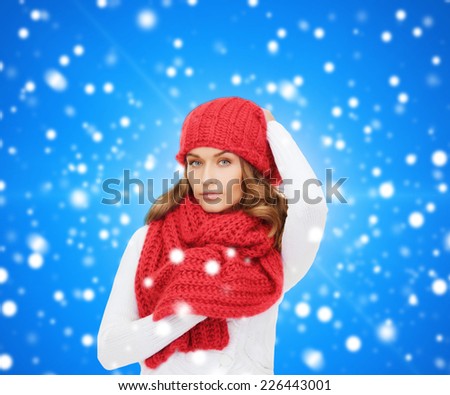 happiness, winter holidays, christmas and people concept - young woman in red hat and scarf over blue snowy background