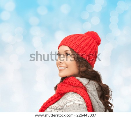 happiness, winter holidays, christmas and people concept - smiling young woman in red hat and scarf over blue lights background
