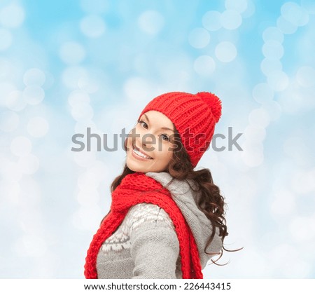 happiness, winter holidays, christmas and people concept - smiling young woman in red hat and scarf over blue lights background