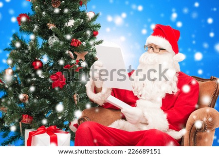 christmas, holidays and people concept - man in costume of santa claus with letter and christmas tree sitting in armchair over blue snowy background