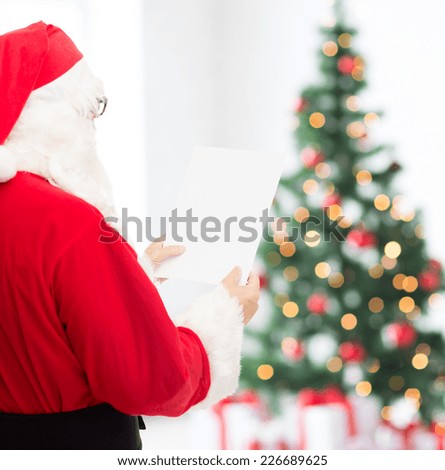christmas, holidays and people concept - man in costume of santa claus reading letter over living room with tree background