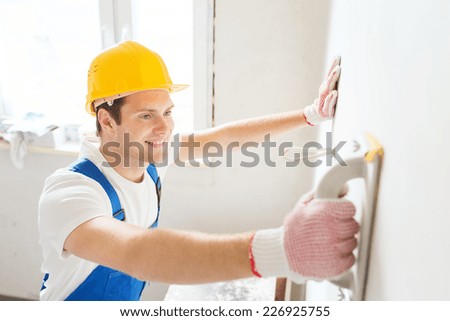 business, building, profession and people concept - smiling builder with grinding tool indoors