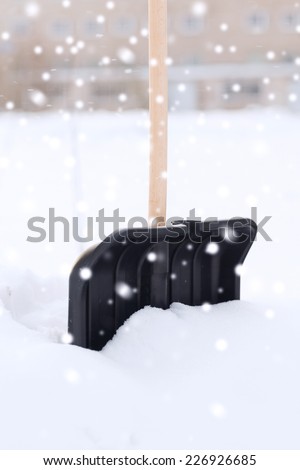 winter and equipment concept - black snowshowel with wooden handle in snow pile