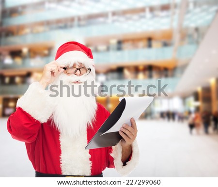 christmas, holidays and people concept - man in costume of santa claus with notepad over shopping center background