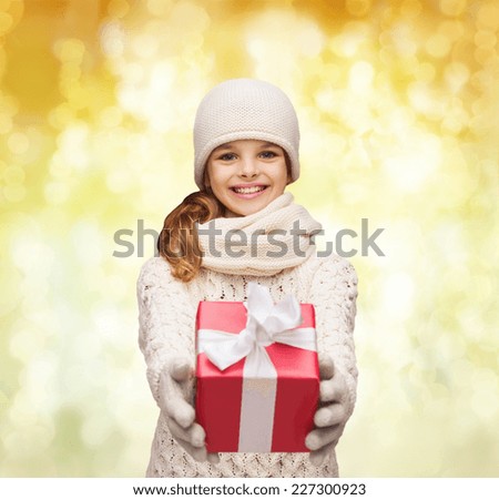 christmas, holidays, childhood, presents and people concept - dreaming girl in winter clothes with gift box over yellow lights background