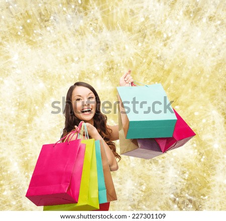 sale, gifts, holidays and people concept - smiling woman with colorful shopping bags over yellow lights background