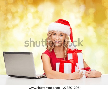 christmas, holidays, technology and people concept - smiling woman in santa helper hat with gifts and laptop computer over yellow lights background