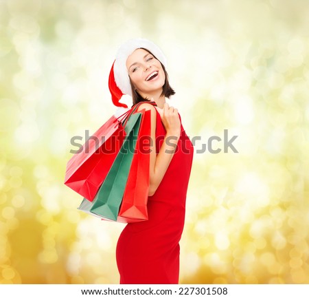 sale, gifts, christmas, holidays and people concept - smiling woman in red dress with shopping bags over yellow lights background
