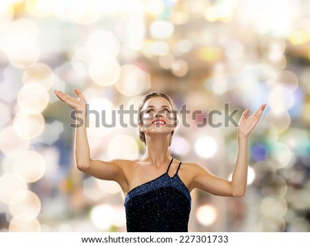 people, happiness, holidays and glamour concept - smiling woman raising hands and looking up over lights background