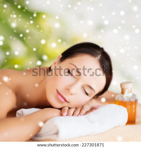 beauty, health, people and spa concept - beautiful young woman with body oil in spa over green background
