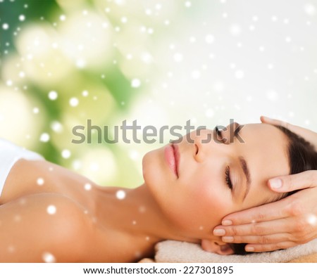 beauty, health, holidays, people and spa concept - beautiful woman in spa salon getting face or head massage over green background