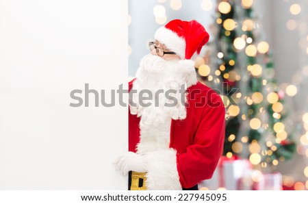 christmas, holidays, advertisement and people concept - man in costume of santa claus with white blank billboard over tree lights background