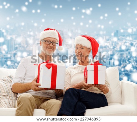 family, holidays, christmas, age and people concept - happy senior couple in santa helper hats with gift boxes over snowy city background