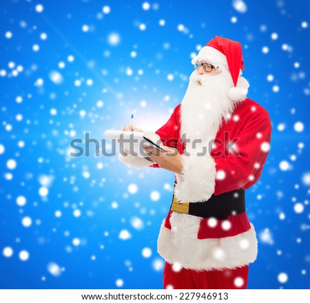christmas, holidays and people concept - man in costume of santa claus with notepad and pen over blue snowy background