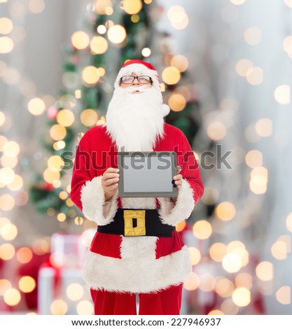 christmas, advertisement, technology, and people concept - man in costume of santa claus with tablet pc computer over tree lights background