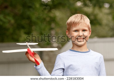 dreams, future, hobby, people and childhood concept - smiling little boy holding wooden airplane model in his hand outdoors