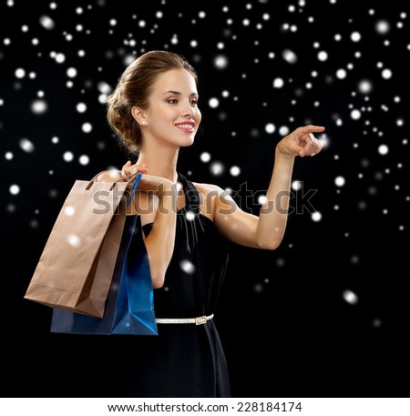 luxury, holydays, people and sale concept - smiling woman with shopping bags over black snowy background