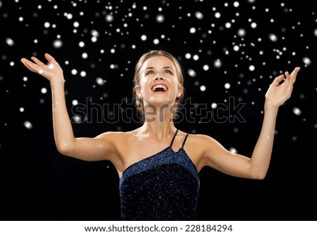 people, happiness, holidays and christmas concept - smiling woman raising hands and looking up over black snowy background