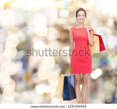 shopping, sale, christmas and holidays concept - smiling elegant woman in red dress with shopping bags over lights background