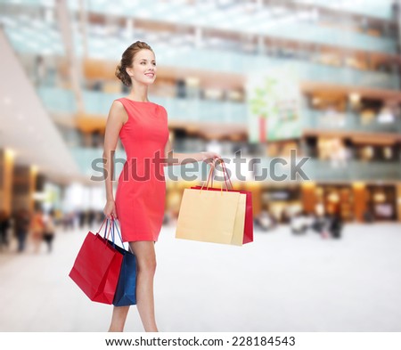 shopping, sale, christmas and holiday concept - smiling elegant woman in red dress with bags over shopping center background
