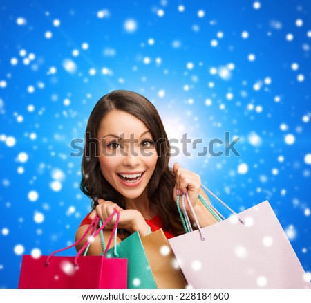sale, gifts, christmas, holidays and people concept - smiling woman with colorful shopping bags over blue snowy background