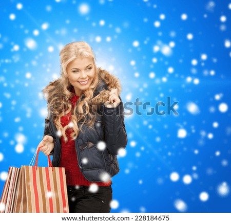 happiness, winter holidays, christmas and people concept - smiling young woman in winter clothes with shopping bags over blue snowy background
