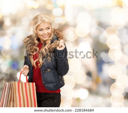 happiness, winter holidays, christmas and people concept - smiling young woman in winter clothes with shopping bags over lights background