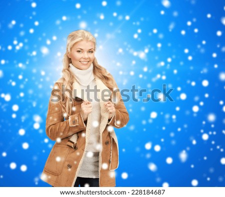 winter holidays, christmas, fashion and people concept - smiling young woman in winter clothes over blue snowy background