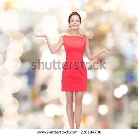 advertising, holidays and people concept - smiling young woman in red dress holding something on palm of her hands over lights background