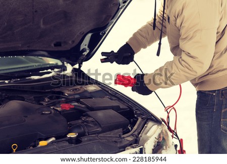 transportation, winter and vehicle concept - closeup of man under bonnet with starter cables
