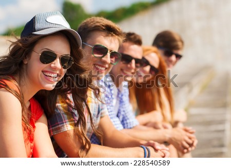 friendship, leisure, summer and people concept - close up of smiling friends sitting on city street