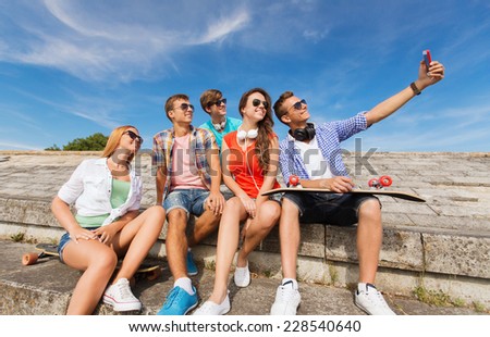 friendship, leisure, summer, technology and people concept - group of smiling friends with skateboard and smartphone making selfie outdoors