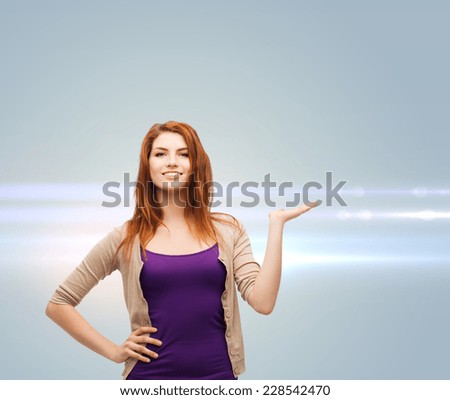 future, advertising and people concept - smiling teenage girl in casual clothes holding something on her palm over gray background with laser light